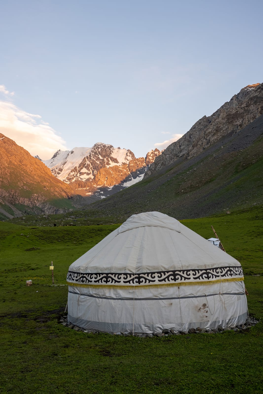 White yurt on a green meadow at dusk with alpenglow on the peaks behind