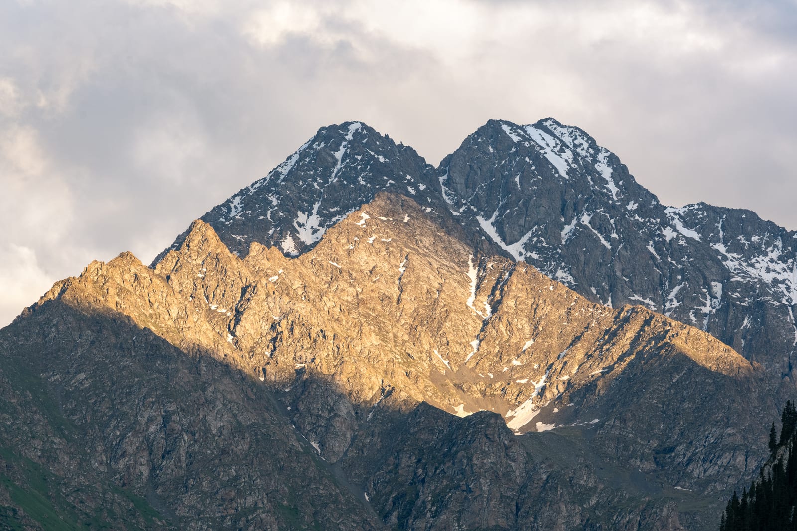Band of golden light across a rocky snow-dusted peak under grey cloud