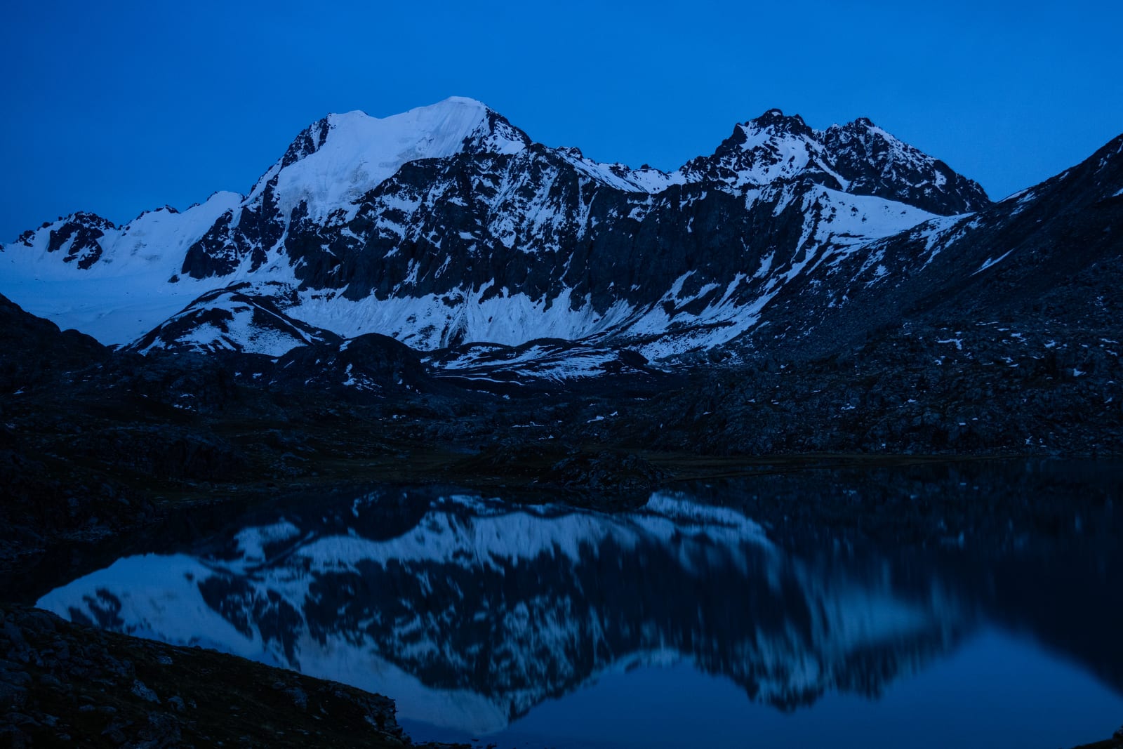 Deep blue-hour view of snowy peaks reflected in an alpine lake