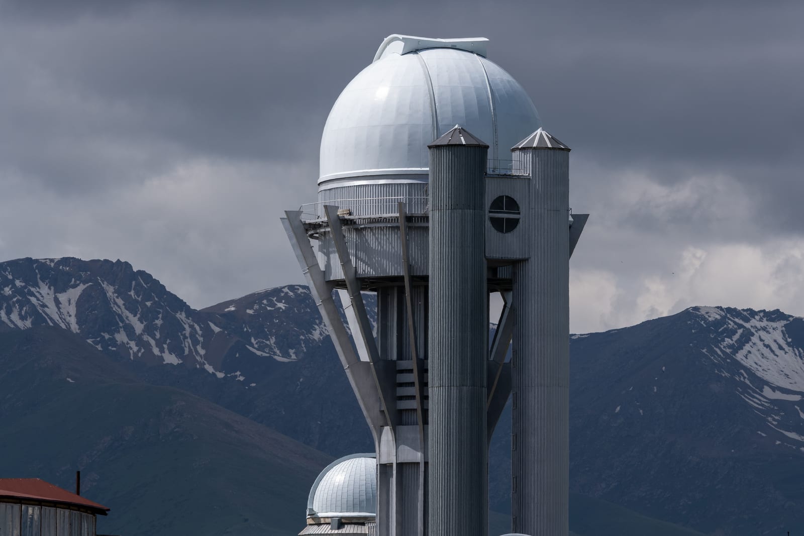 Observatory dome tower against dark storm cloud and snowy mountains