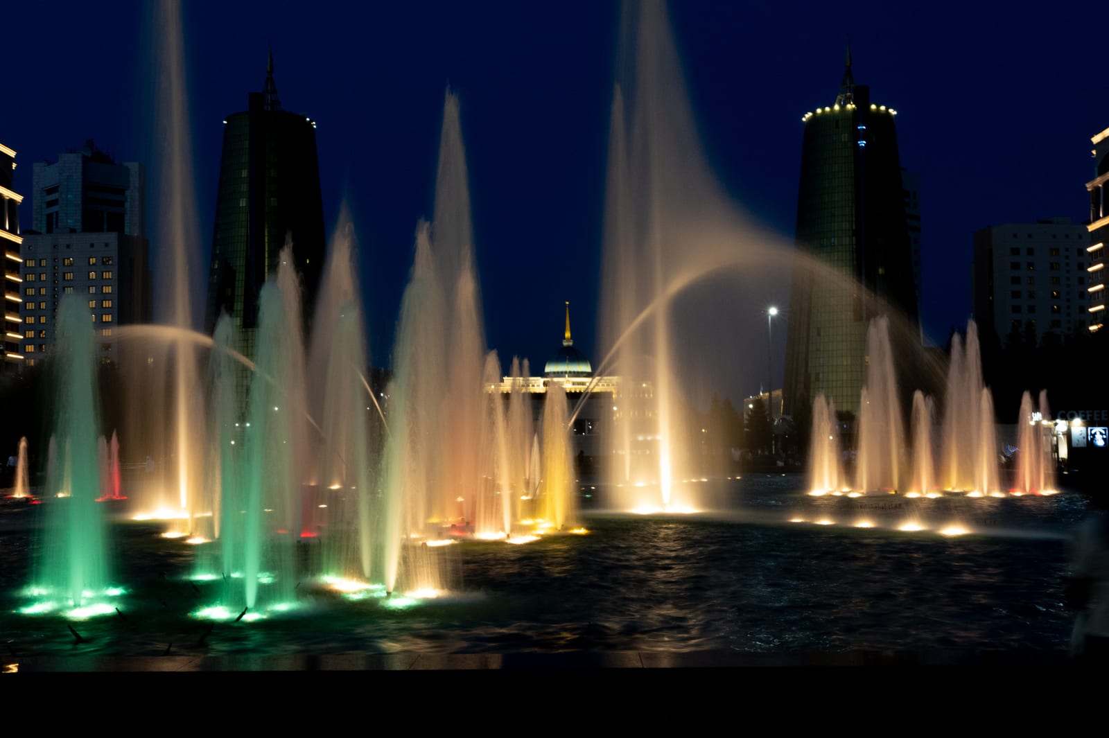 Coloured illuminated fountains at night with towers behind