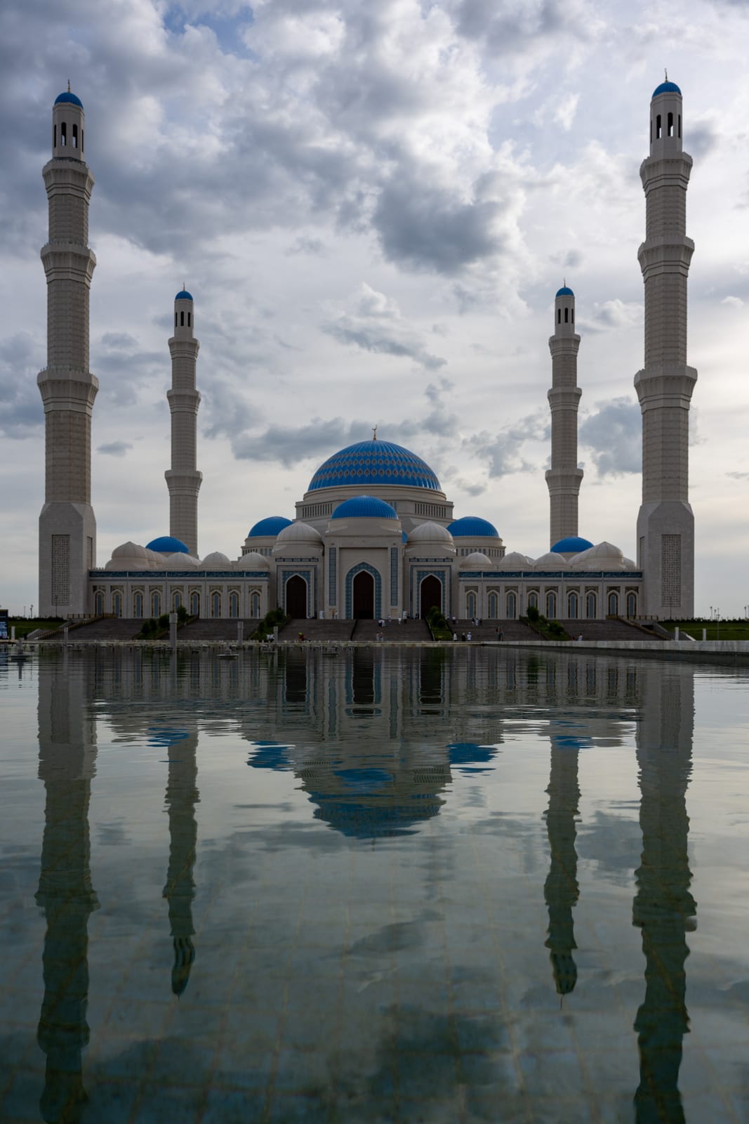 Grand mosque with blue domes and four minarets mirrored in a reflecting pool