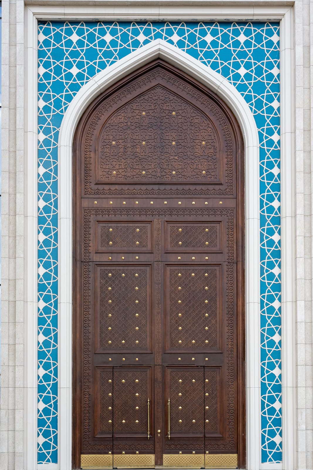 Carved wooden door set in a pointed arch of blue and white geometric tile
