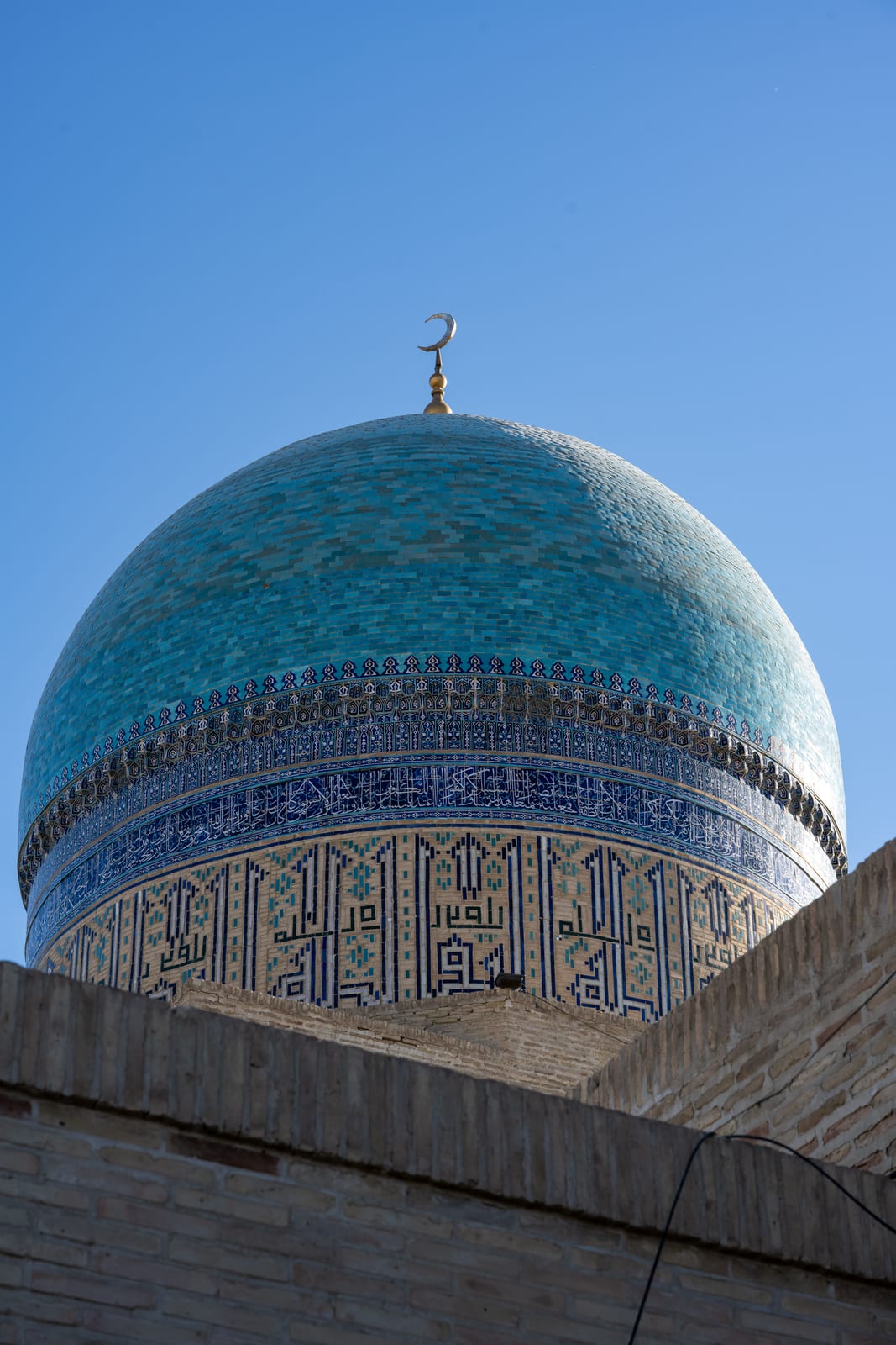 Turquoise tiled dome with calligraphy band against blue sky