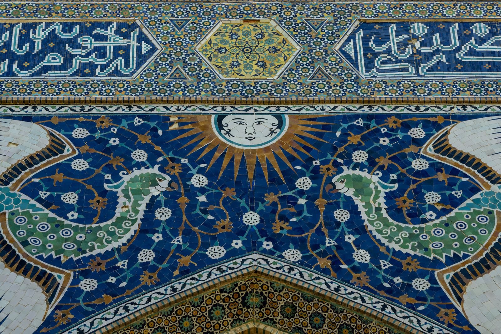 Tilework detail with a sun face and two green birds on a deep blue floral ground