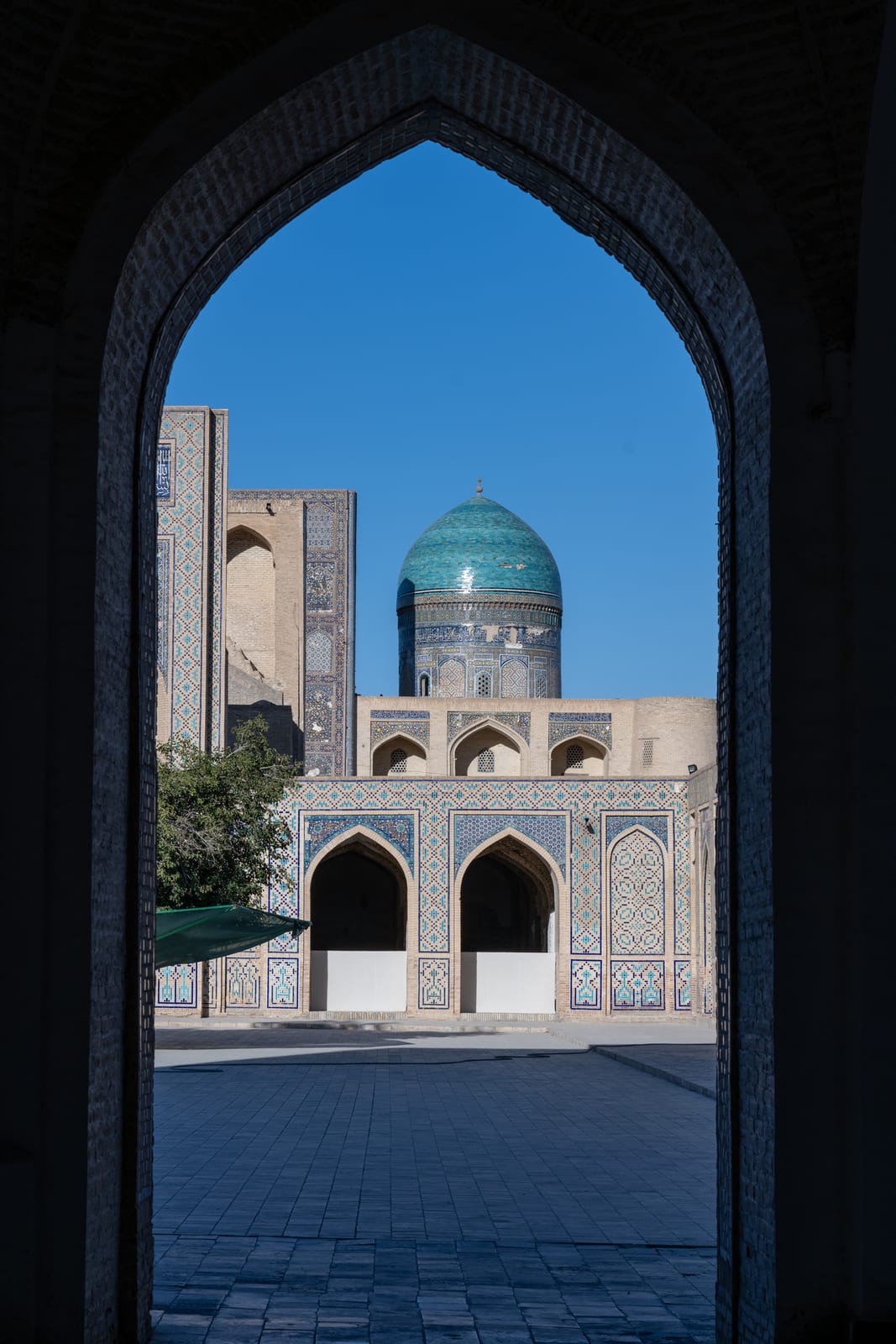 Turquoise dome and courtyard framed through a dark pointed archway