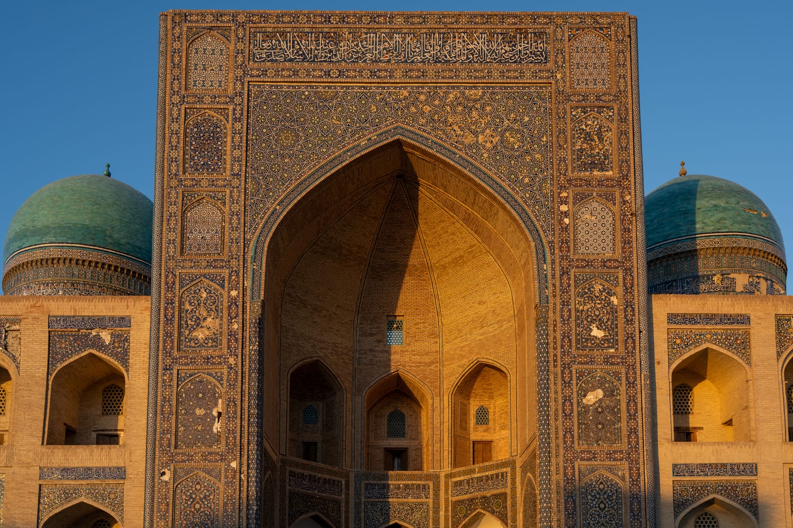 Madrasa portal and twin turquoise domes in warm golden light