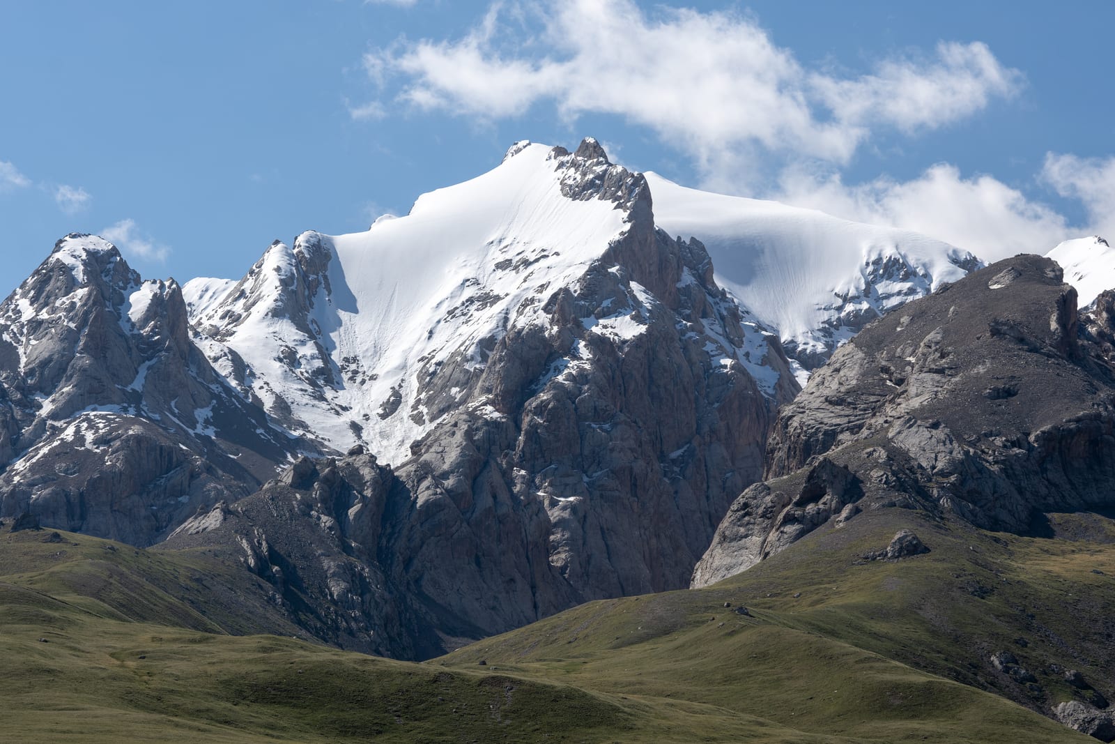 Snow-capped rocky peak with cloud streaming off the summit above green foothills