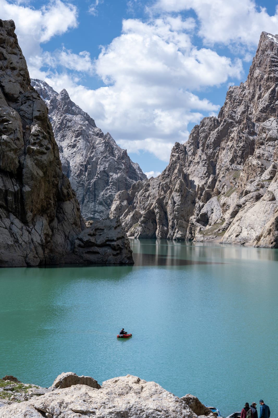 Turquoise lake between sheer grey cliffs with a tiny boat for scale