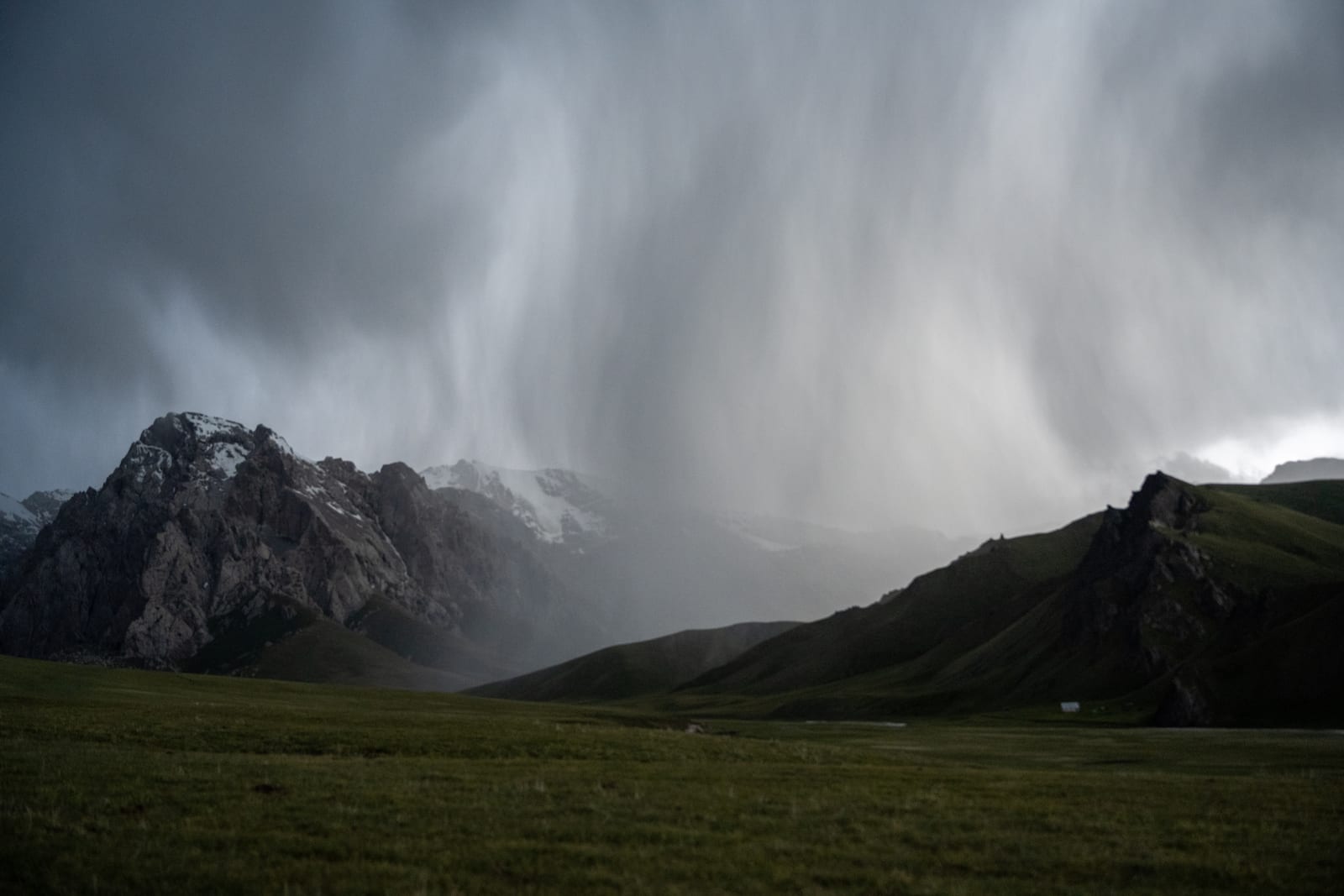 Curtain of rain sweeping across dark mountains and open grassland
