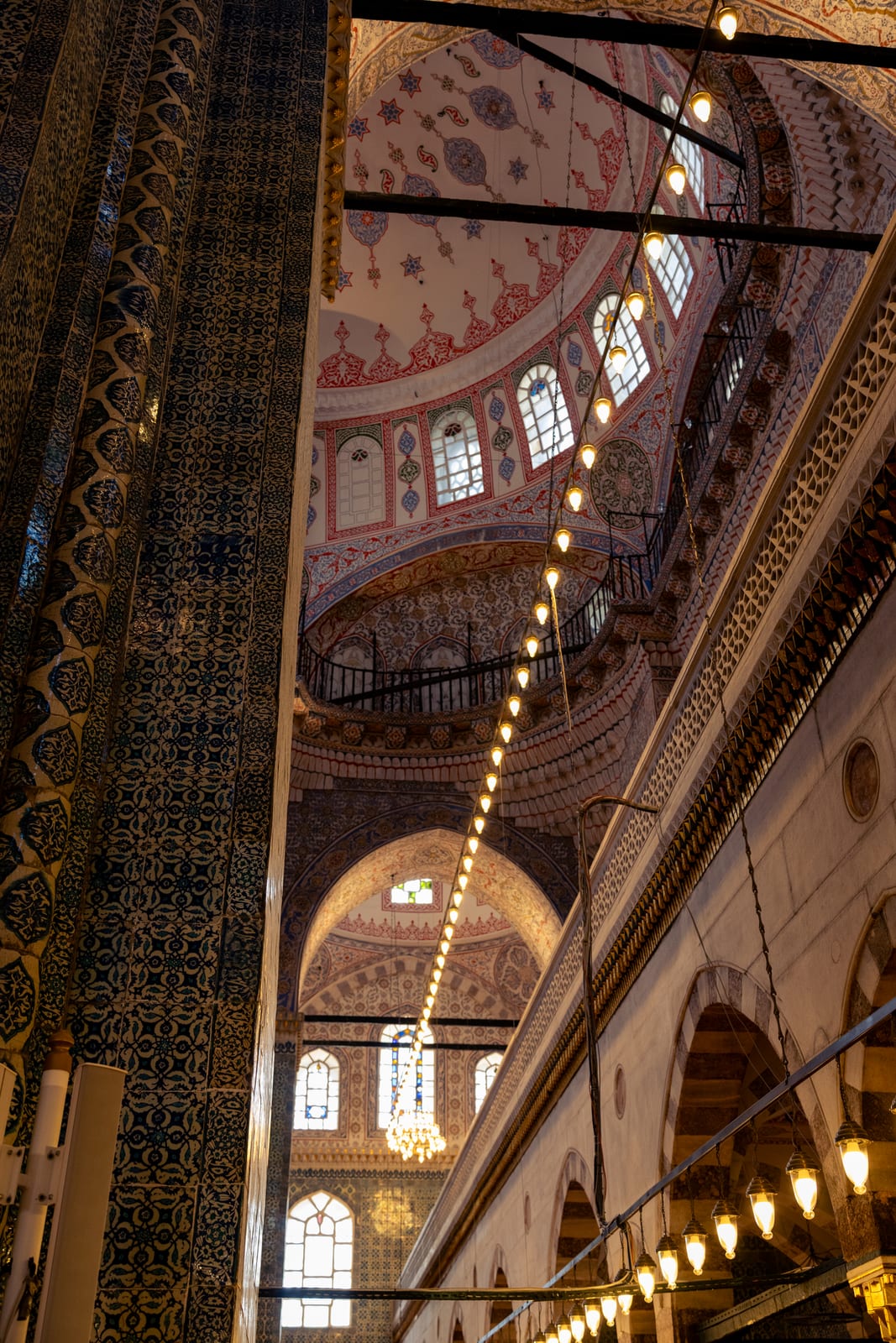 Mosque interior with a diagonal chain of hanging lamps under painted arches, warm light