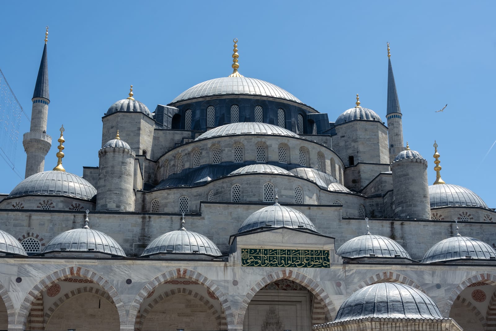 Cascading grey domes and minarets of the Blue Mosque from its courtyard under clear sky