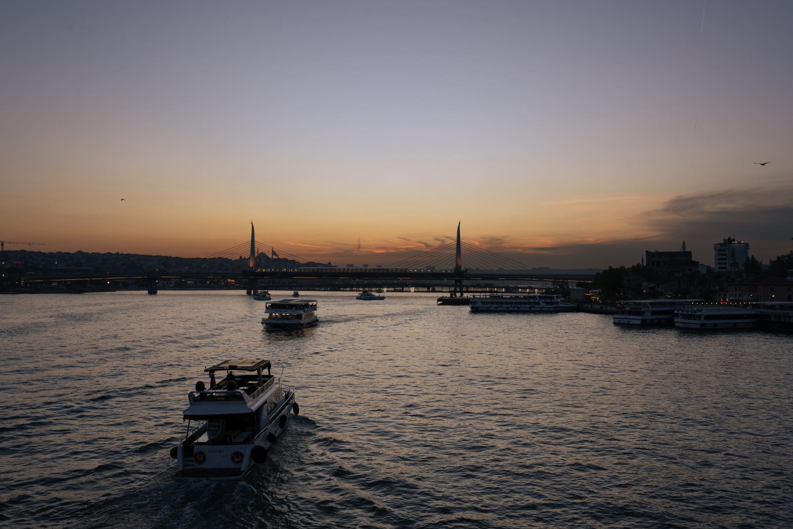 Boats crossing the Golden Horn at dusk, orange afterglow on the horizon, dark rippled water