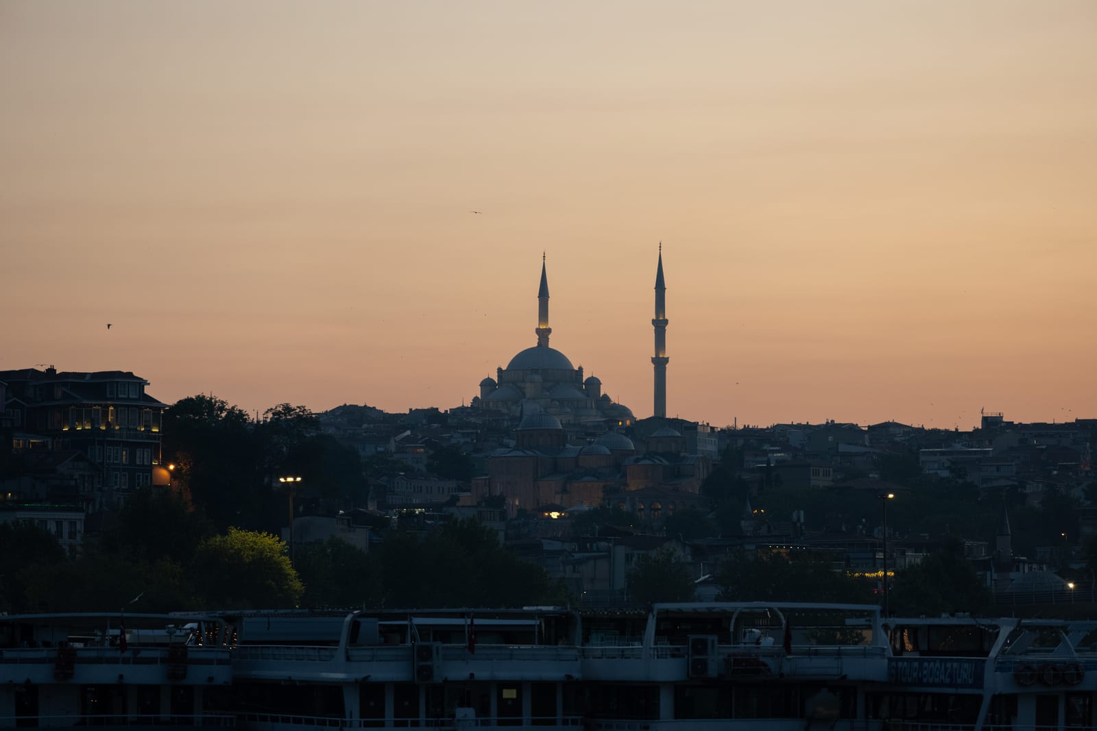 Silhouette of a mosque with two minarets on the skyline against a peach sunset sky