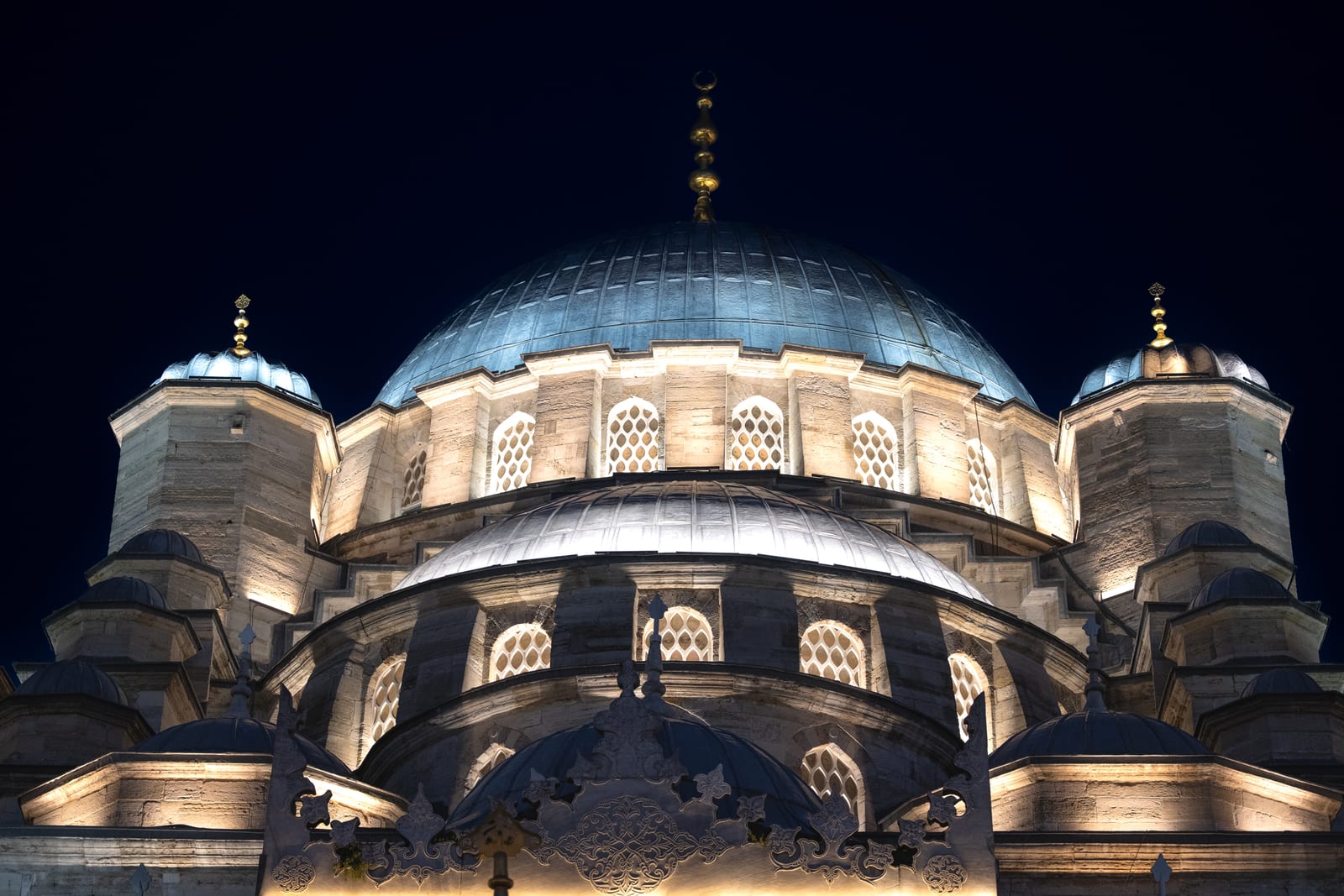 Tight frontal view of an illuminated mosque dome and turrets against black sky