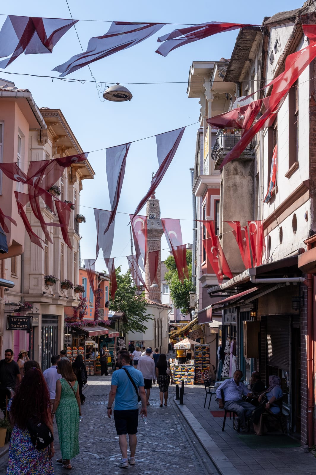 Busy lane of old houses strung with red and white flag bunting, minaret at the end