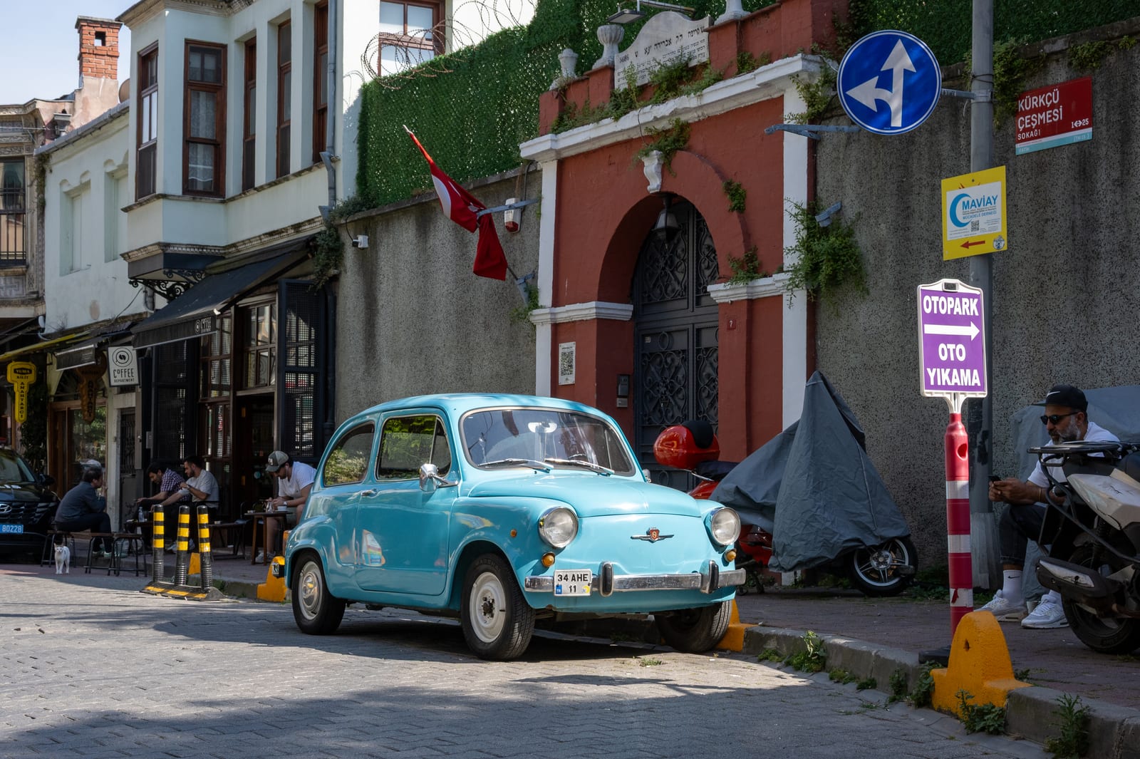 Pale blue vintage microcar parked in front of a red arched gateway on a cobbled street