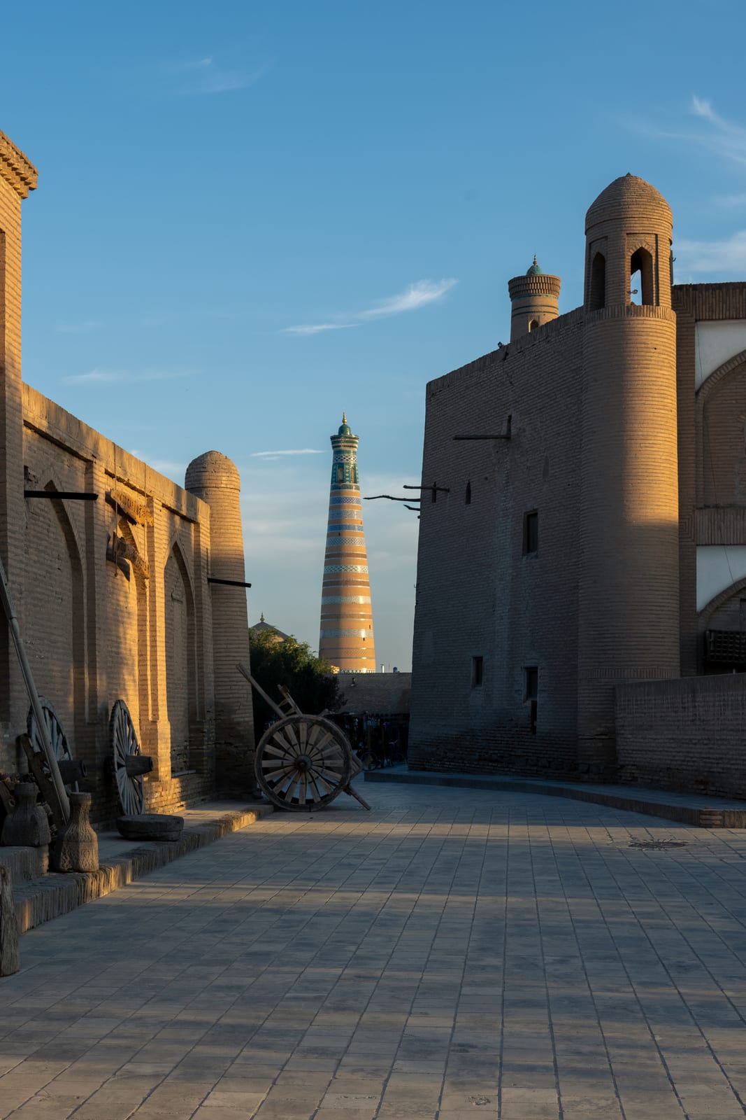 Empty old-town lane at golden hour, mud-brick walls glowing, striped minaret in the distance