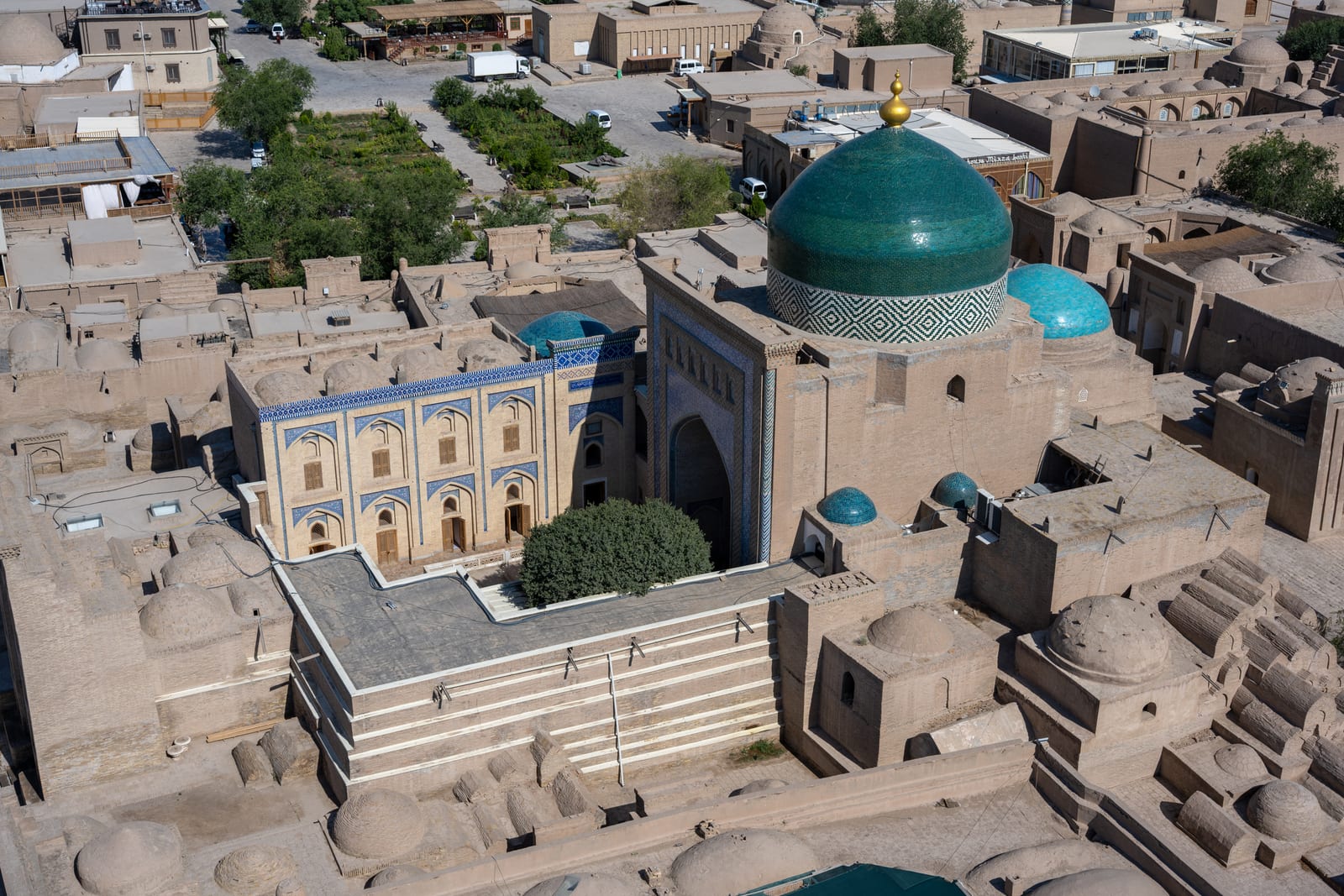 High view over mud-brick rooftops to a turquoise dome and madrasa courtyards