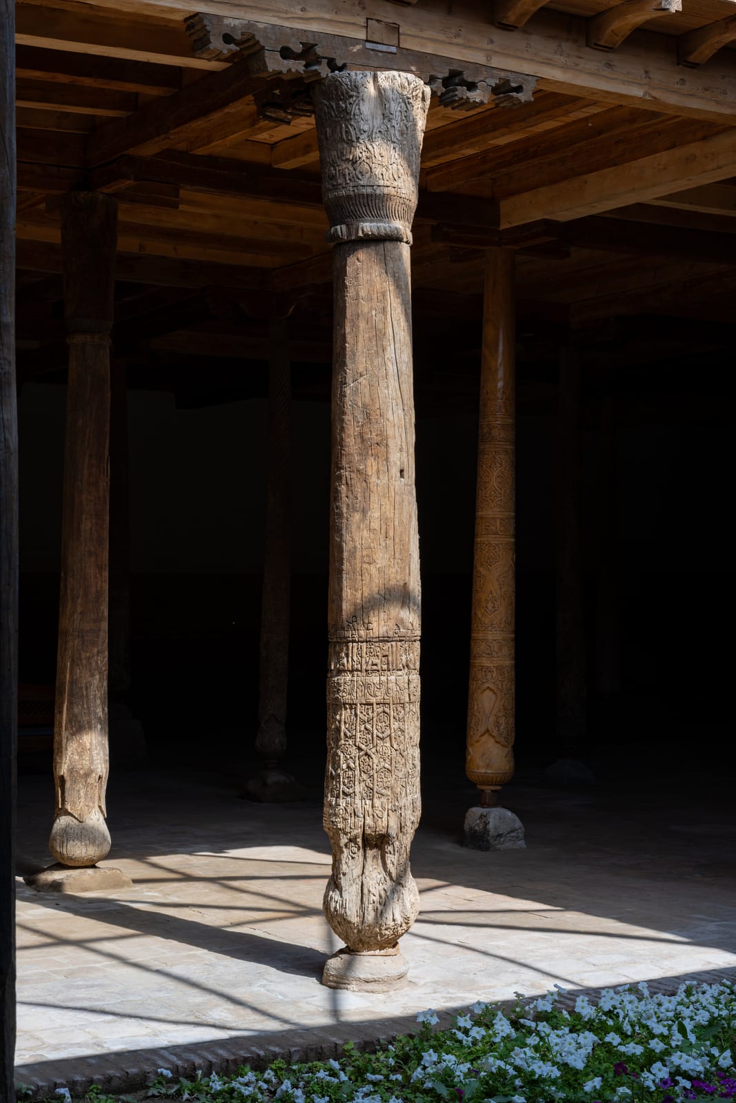Single carved wooden column lit against a dark hall, sunlit floor at its base