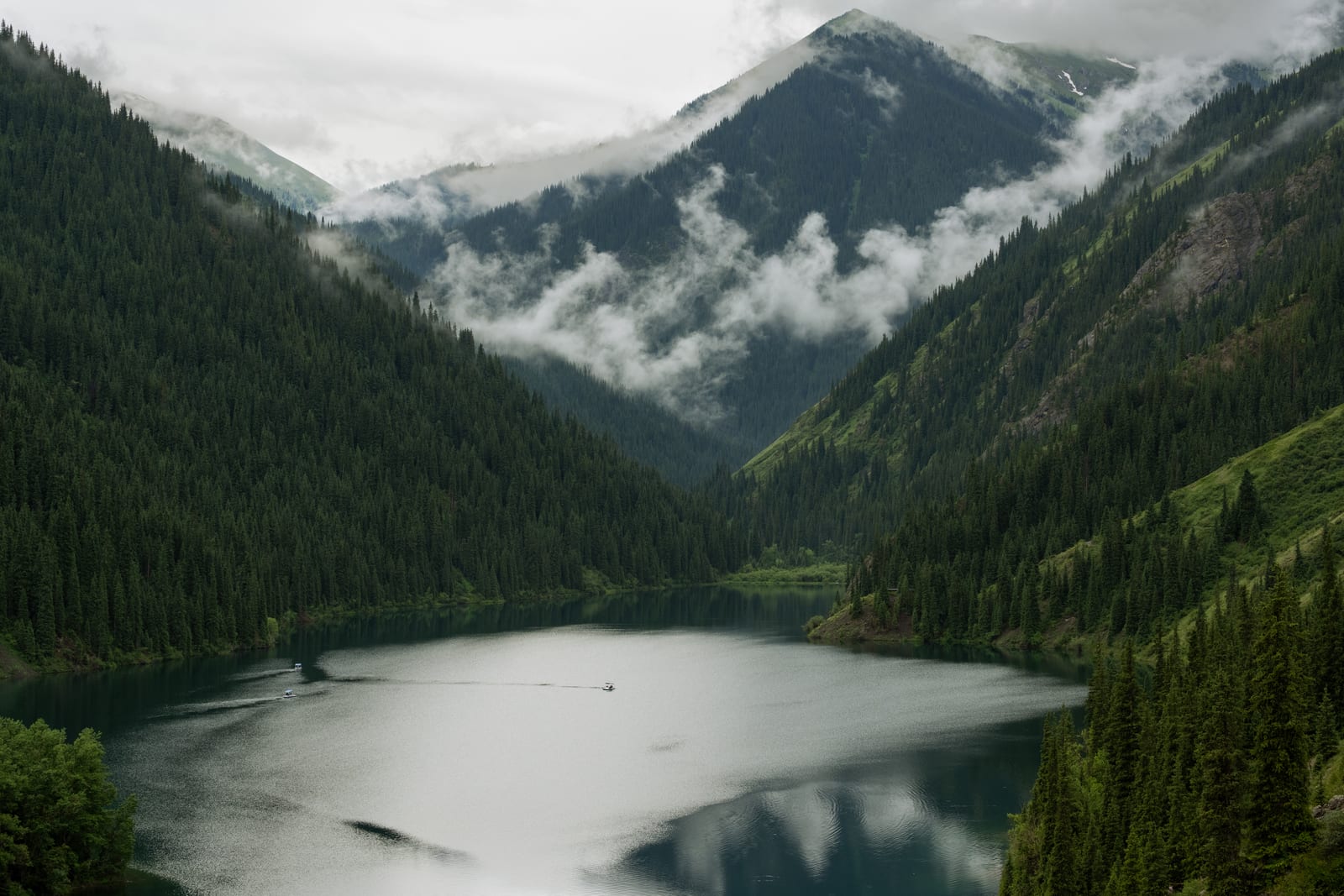 Kolsai lake in a forested valley with cloud wisps clinging to the peaks