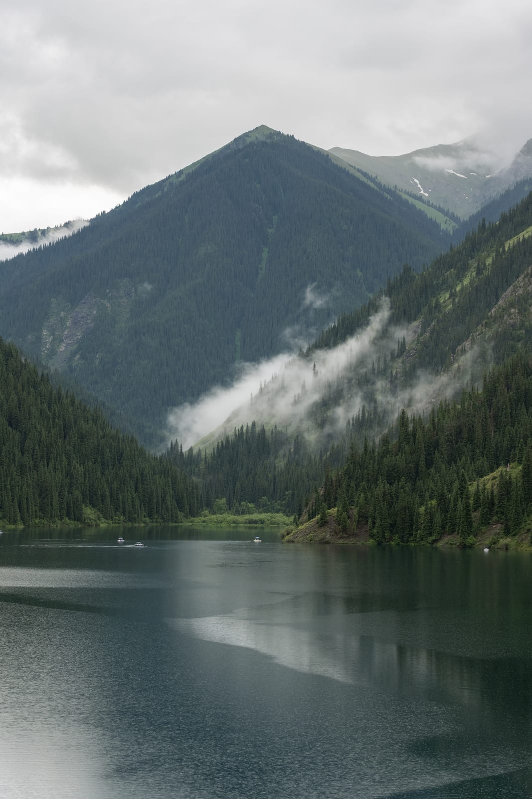 Vertical view of a pyramidal peak and cloud bands reflected in a calm dark lake