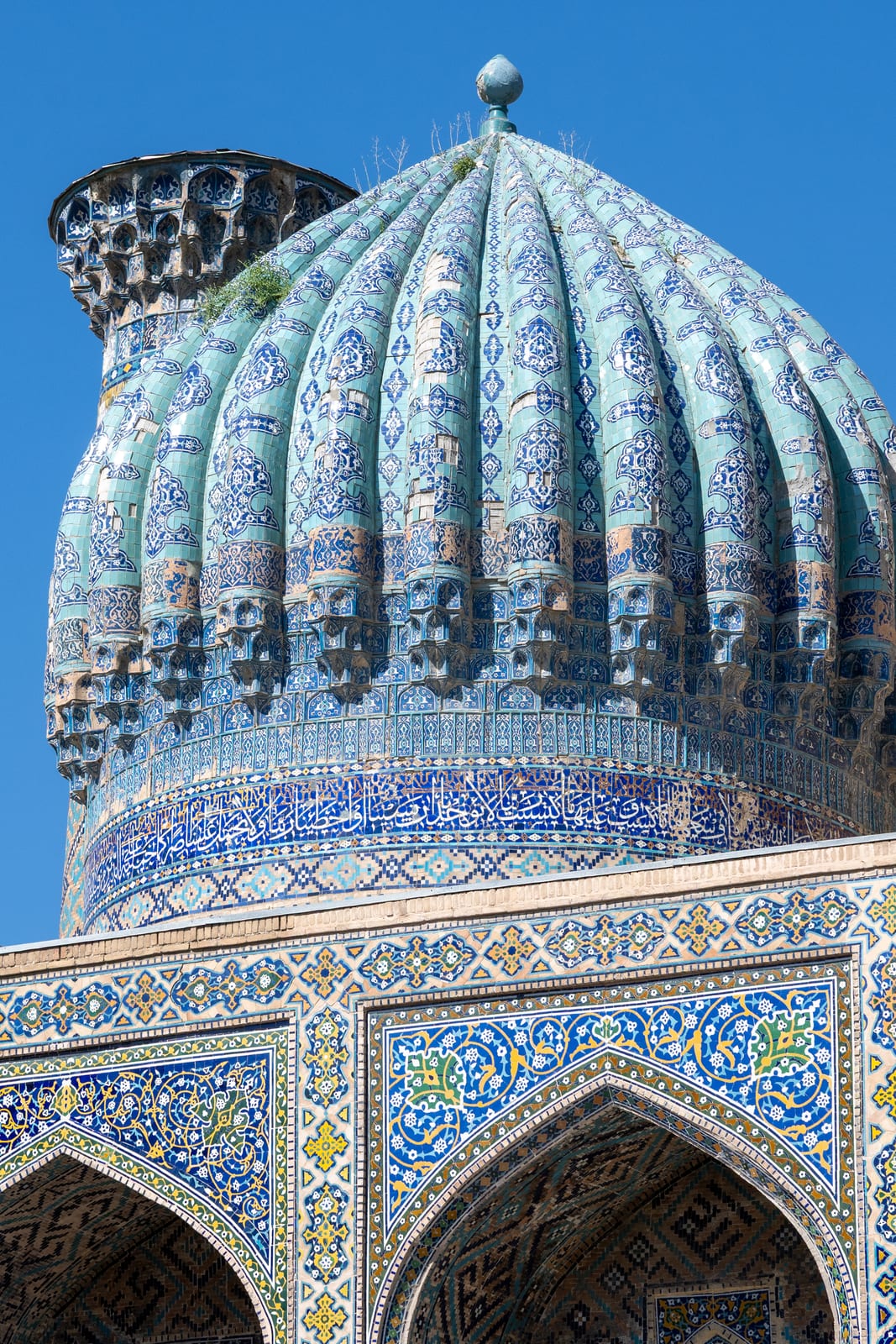 Ribbed blue-tiled dome above tiled arcade arches against clear sky