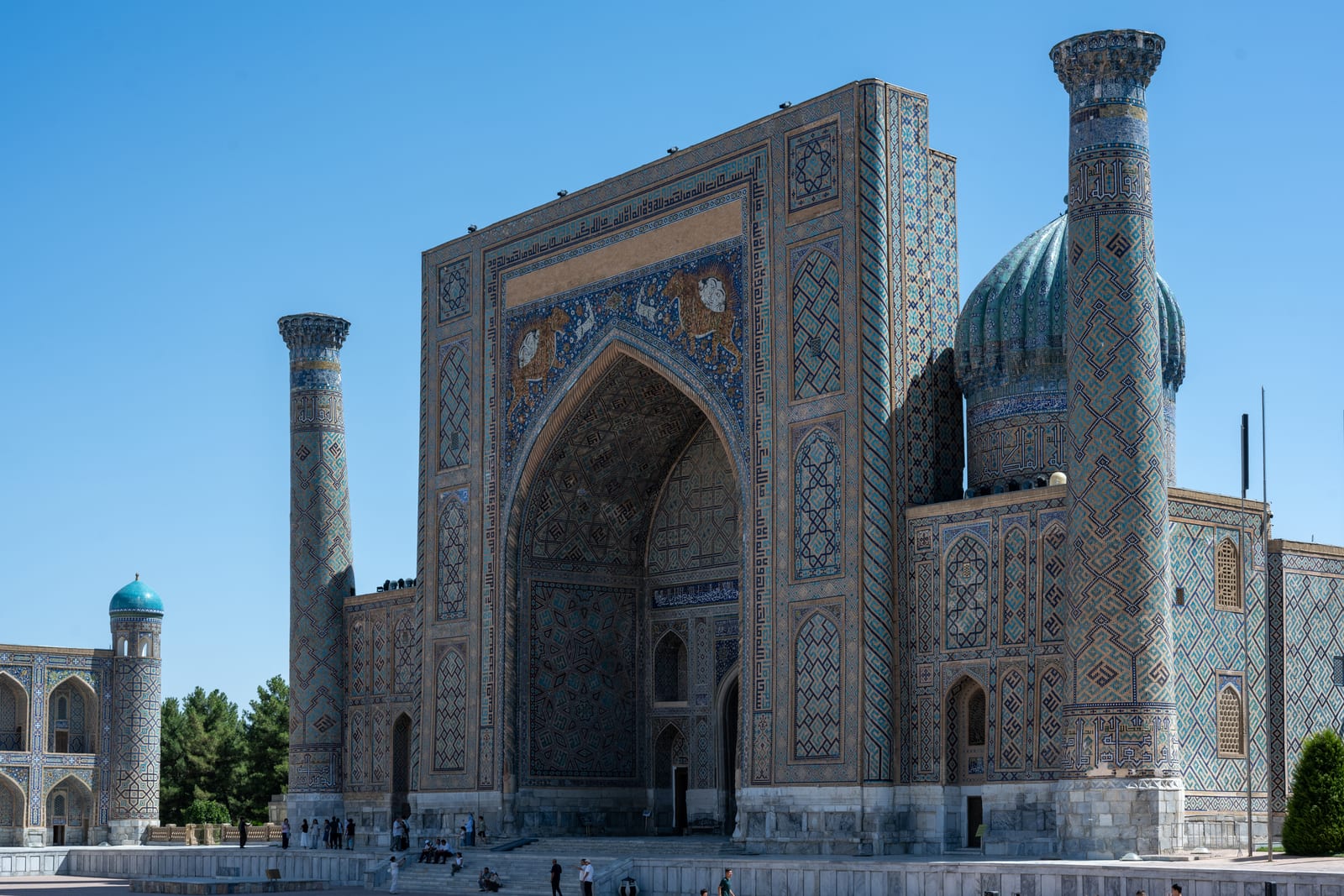 Wide frontal view of a Registan madrasa with leaning minarets and ribbed dome