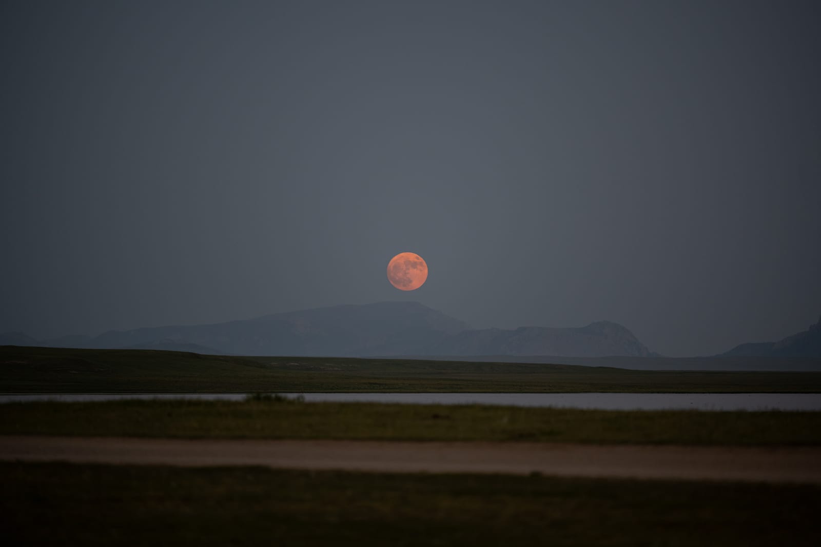 Red full moon rising over a lake and mountain ridge at dusk