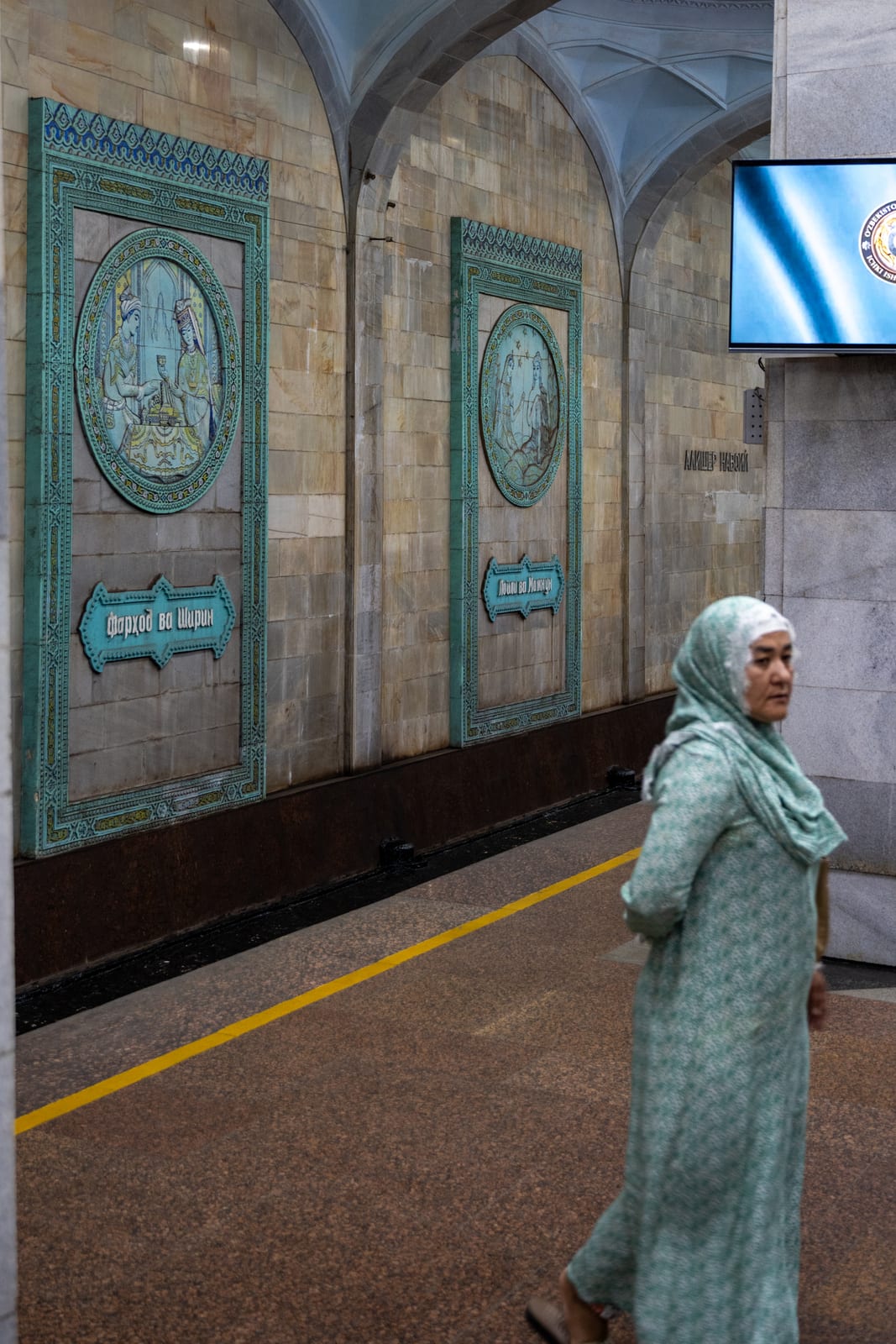 Woman in a green patterned dress and headscarf walking along an ornate metro platform