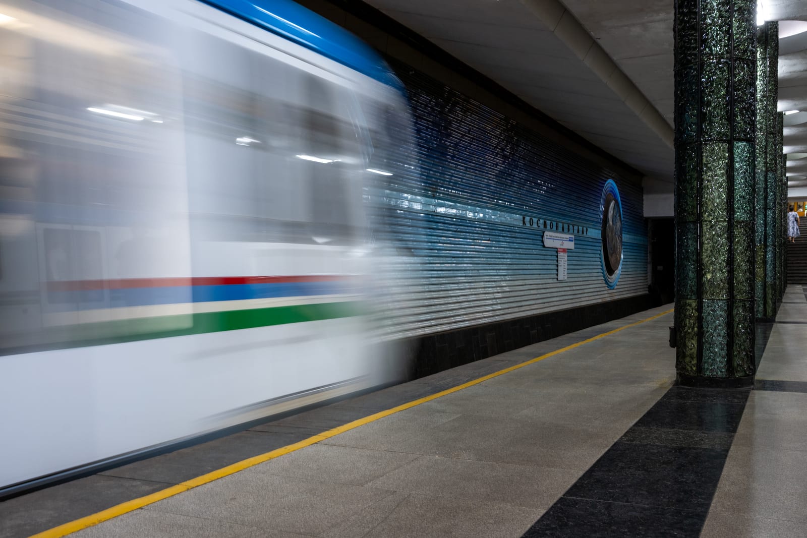 Motion-blurred metro train streaking past a blue tiled station wall and green column