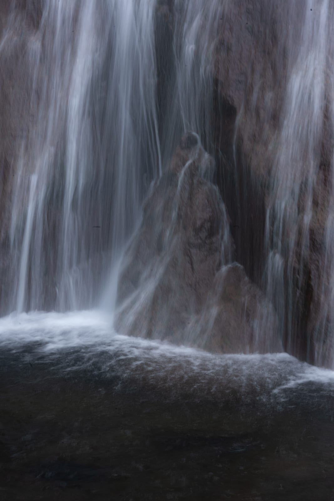 Close long exposure of waterfall veils over reddish rock into a dark pool