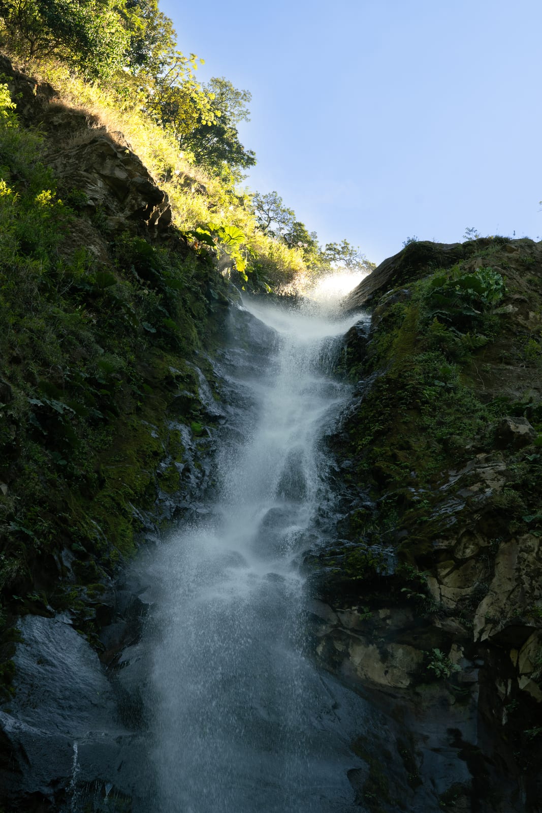 Waterfall dropping through a green gorge under blue sky