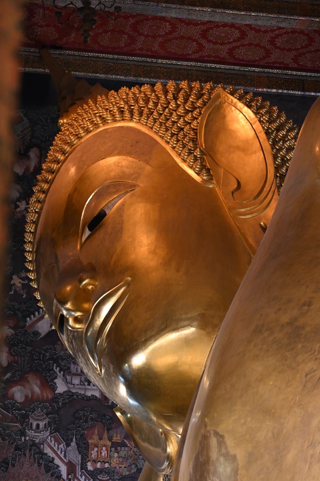Head of the golden Reclining Buddha in profile against dark murals
