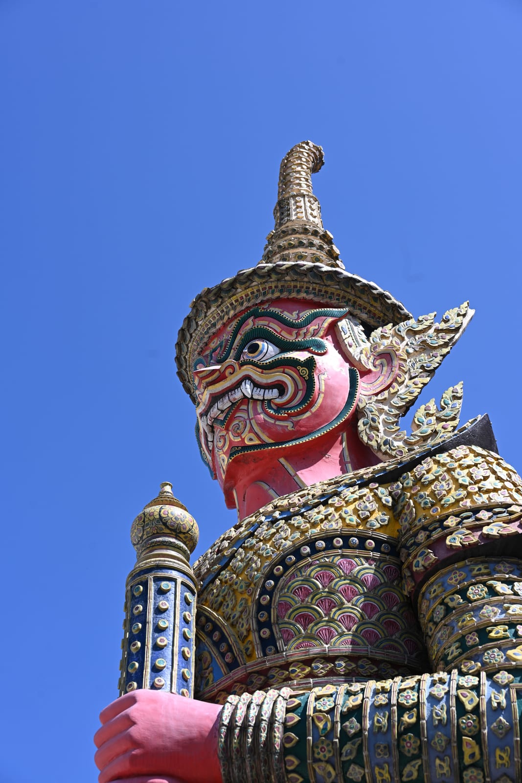 Pink-faced giant yaksha guardian statue against clear blue sky