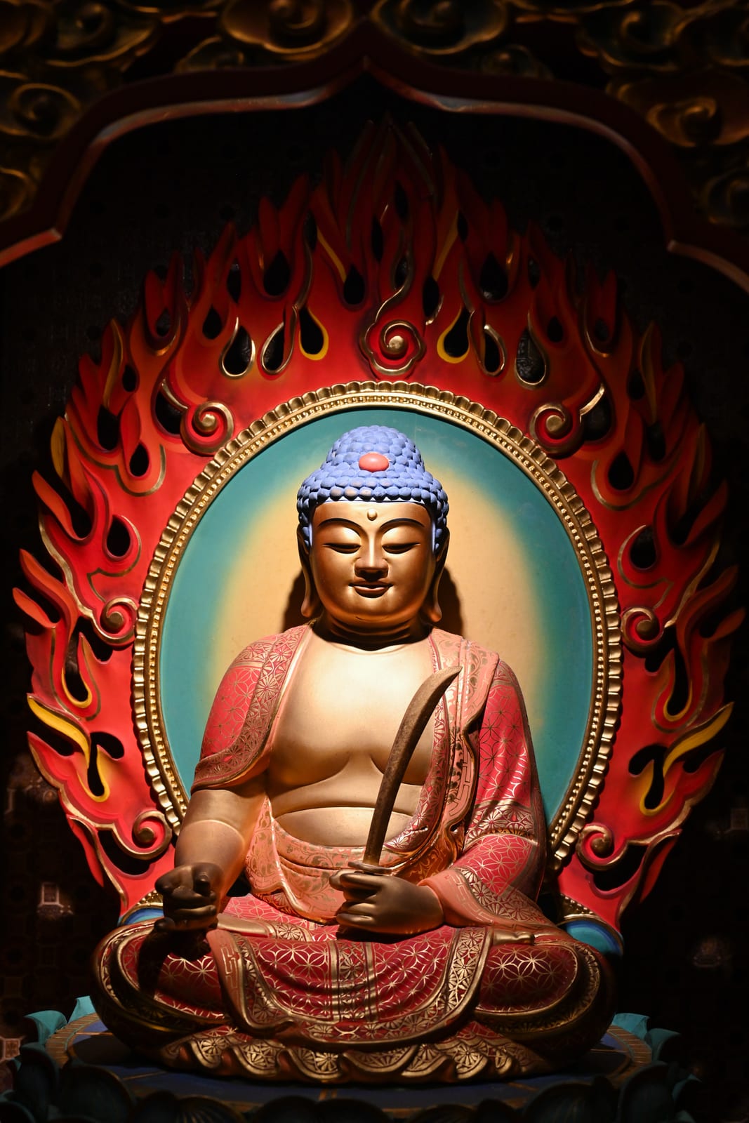 Seated Buddha statue within a red and gold flame mandorla