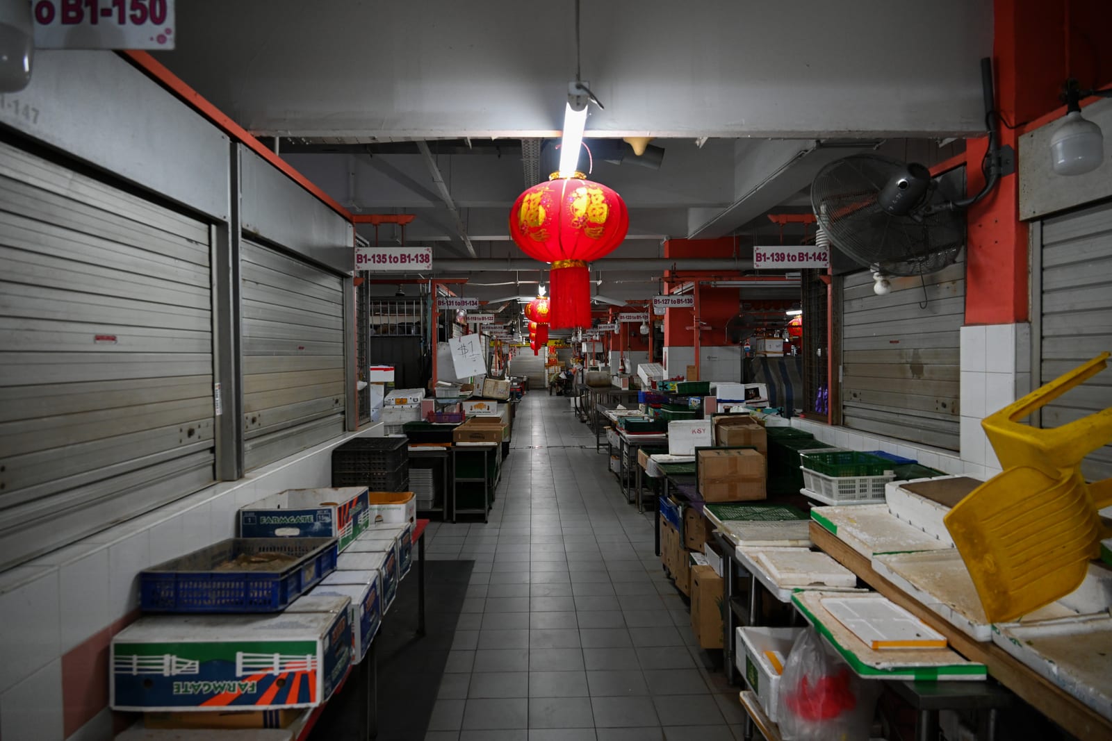 Empty wet-market aisle with a single red lantern under a strip light