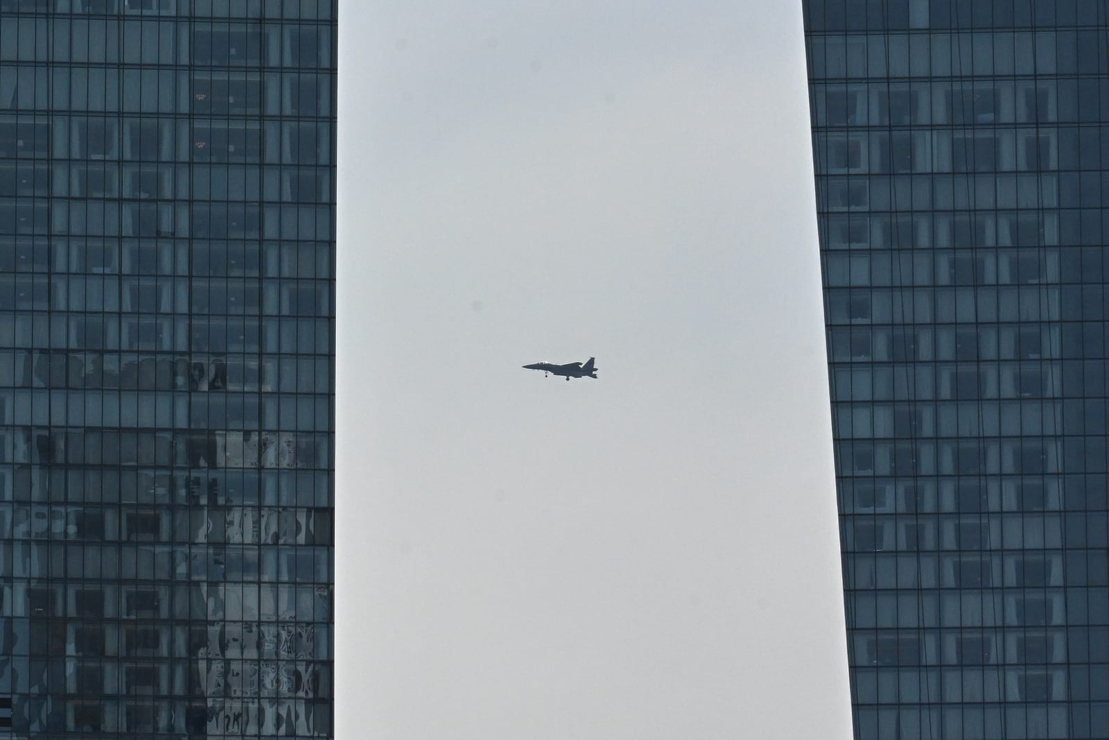 Fighter jet silhouetted in the gap between two glass towers