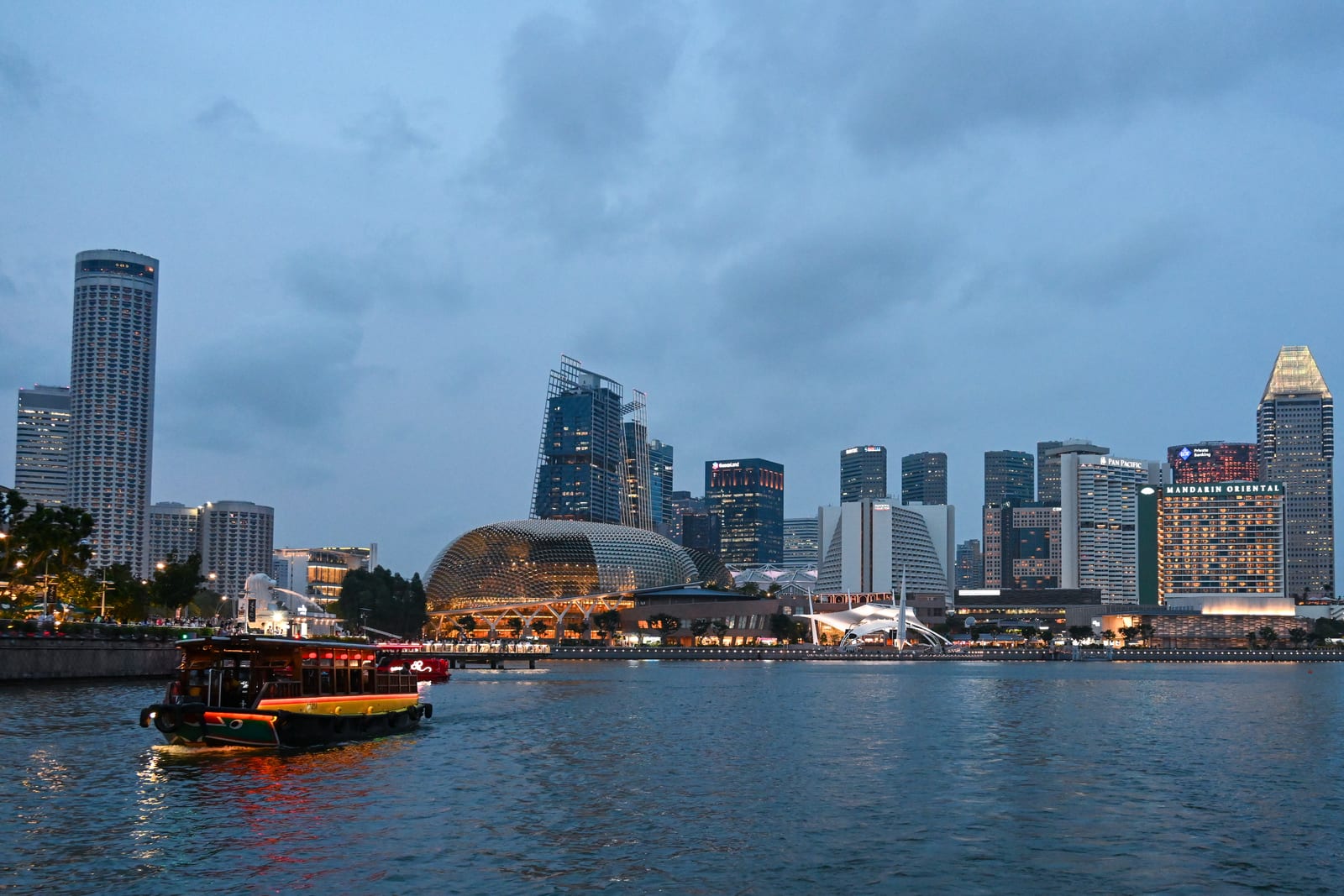 Marina Bay skyline at dusk with a lit bumboat crossing the water