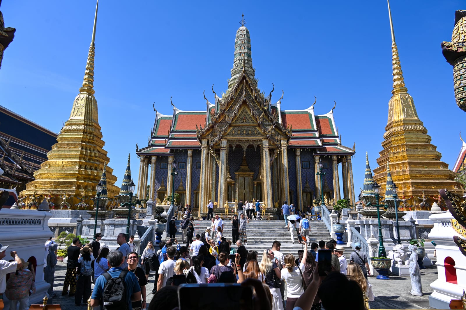 Grand Palace temple hall flanked by two golden chedis with crowd on the steps