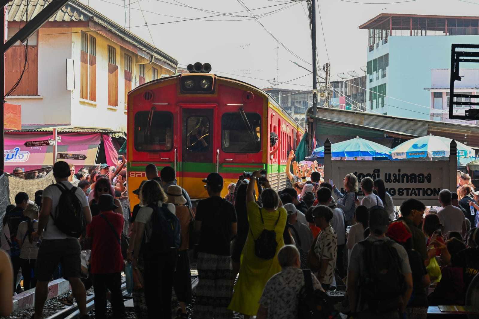 Train arriving through the Maeklong railway market with a crowd of onlookers