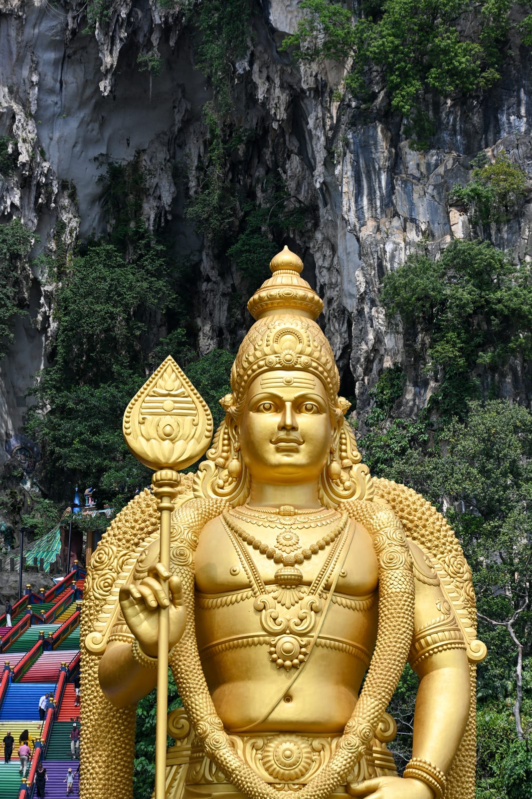 Golden Murugan statue against a limestone cliff and rainbow stairs at Batu Caves