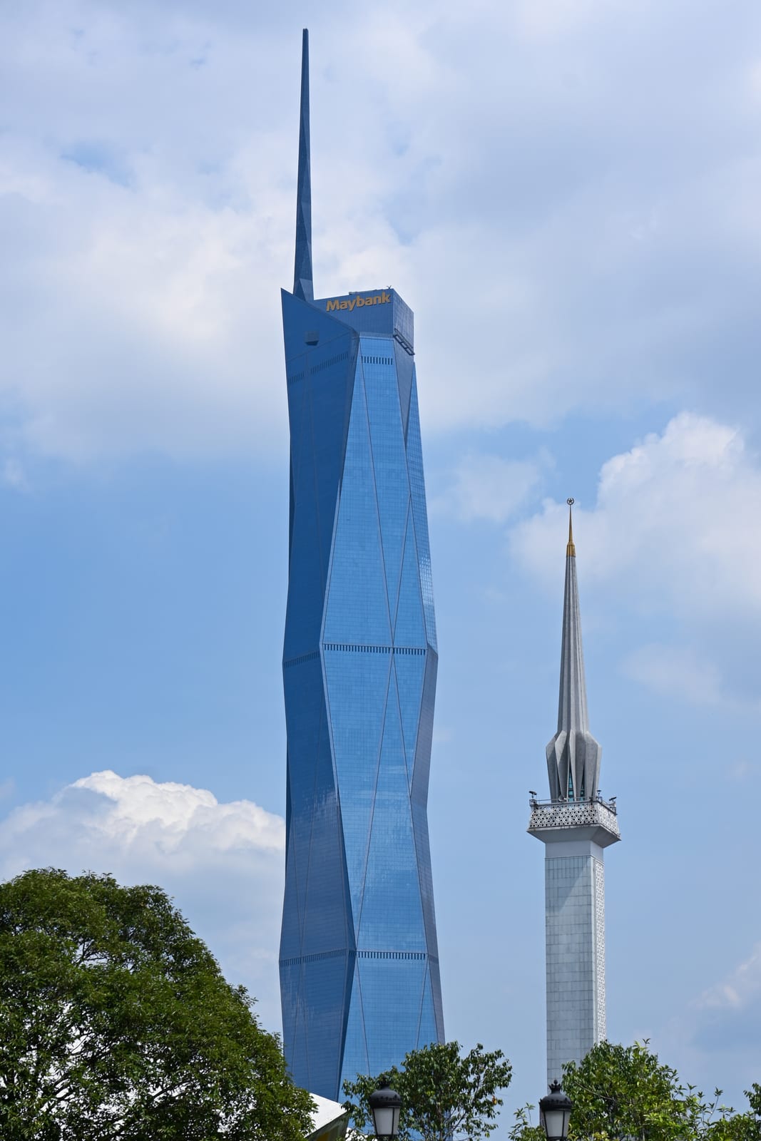 Merdeka 118 tower and a white minaret against blue sky with clouds