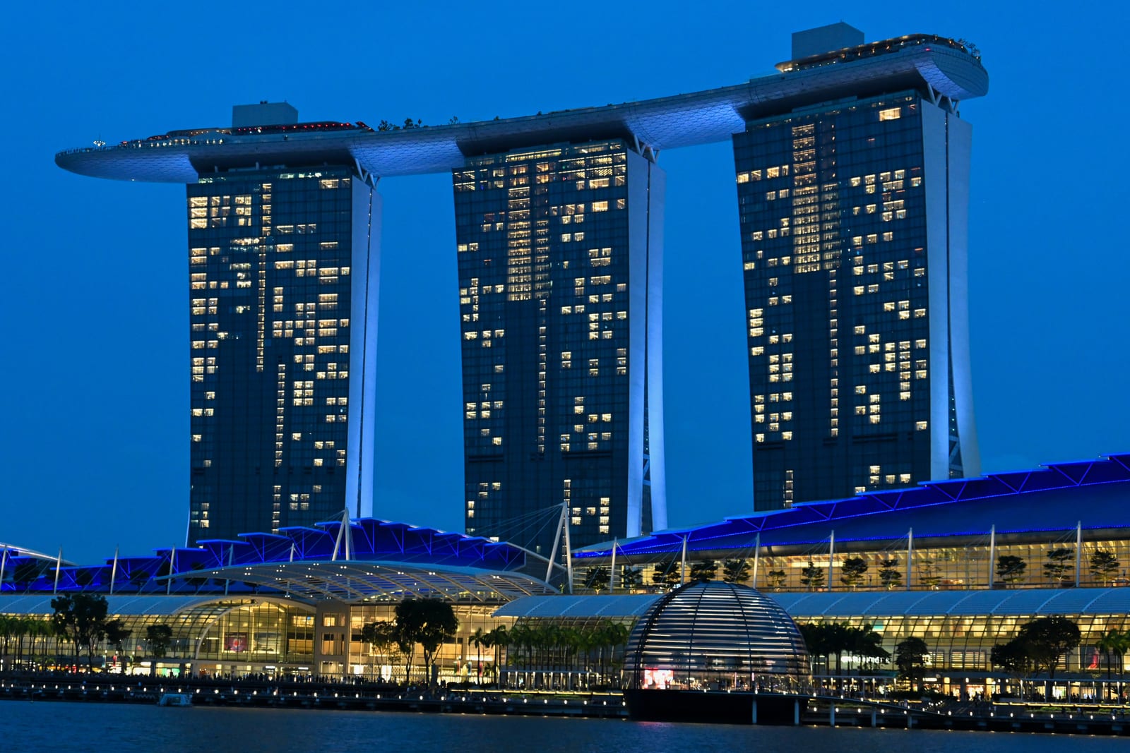 Marina Bay Sands lit at blue hour with glowing waterfront below, deep blue sky