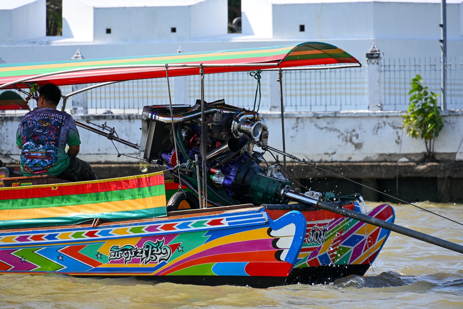 Rainbow-painted longtail boat with its driver and exposed engine on the Chao Phraya