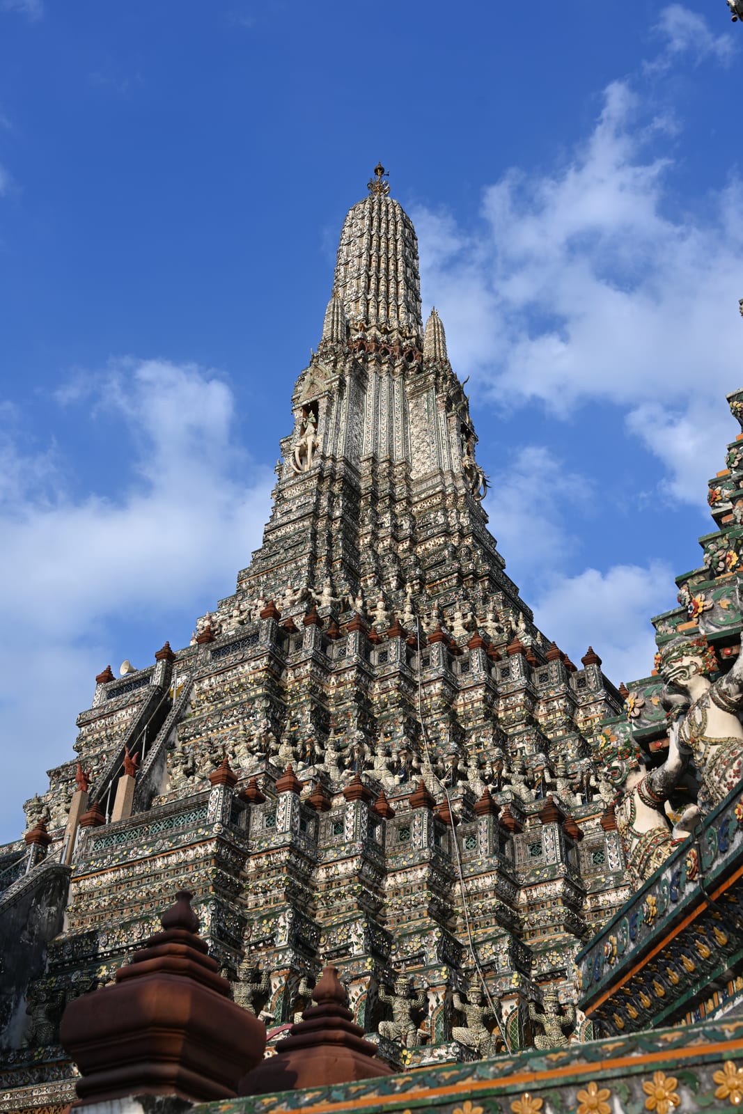 Wat Arun central prang from below against deep blue sky with clouds