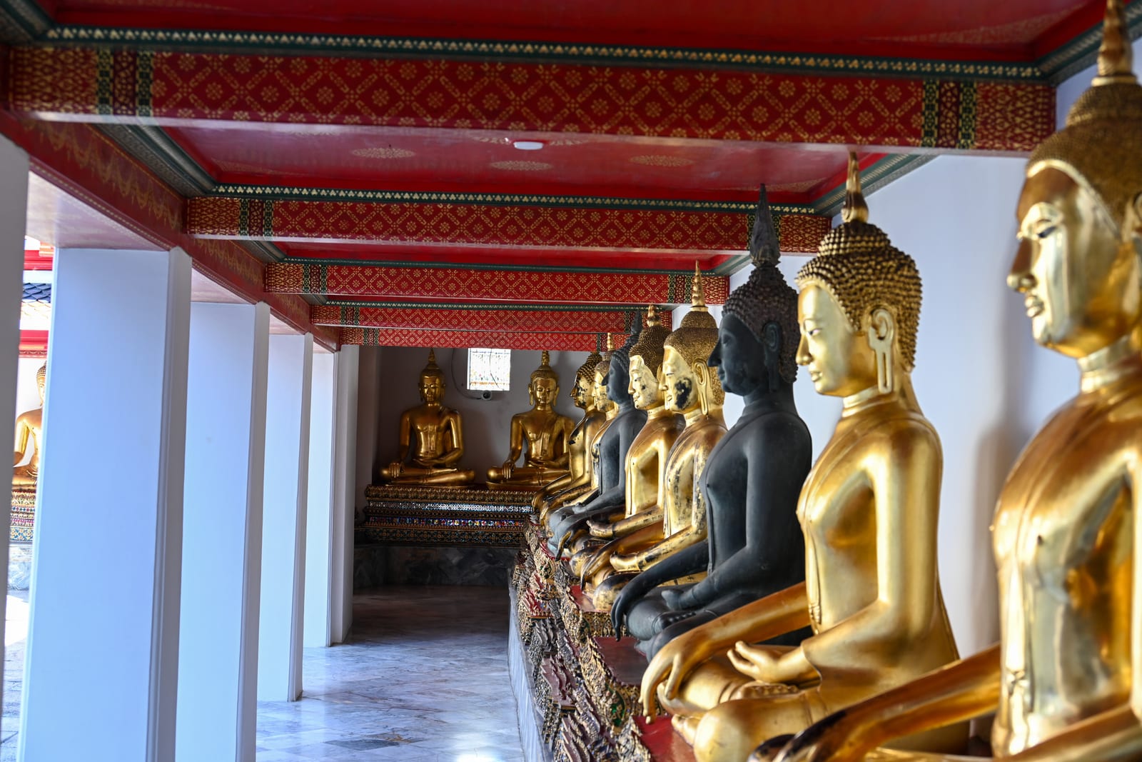 Receding row of gilded seated Buddhas in a red-ceilinged temple cloister
