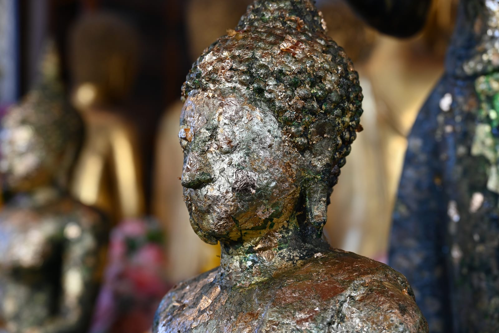 Buddha head covered in flaking gold leaf, shallow focus with gold statues behind