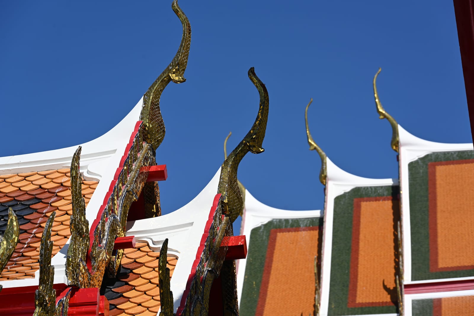 Line of curved temple roof finials and orange tiled gables against blue sky
