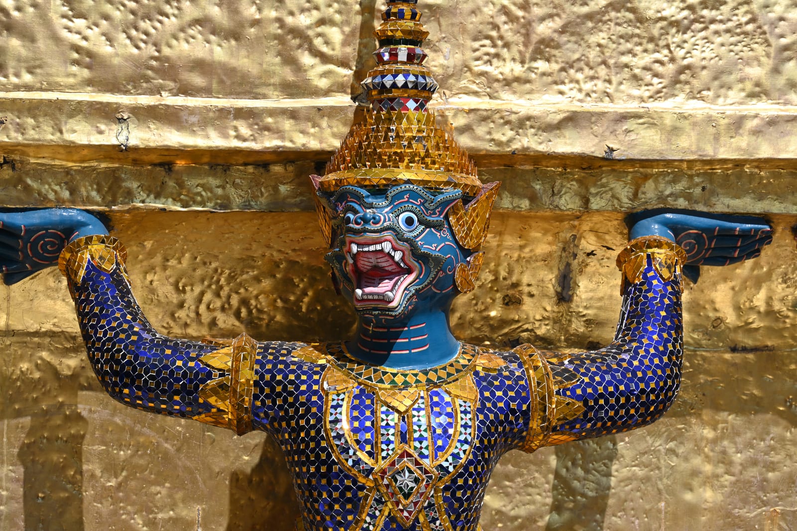 Blue demon figure with arms raised holding up a golden chedi base
